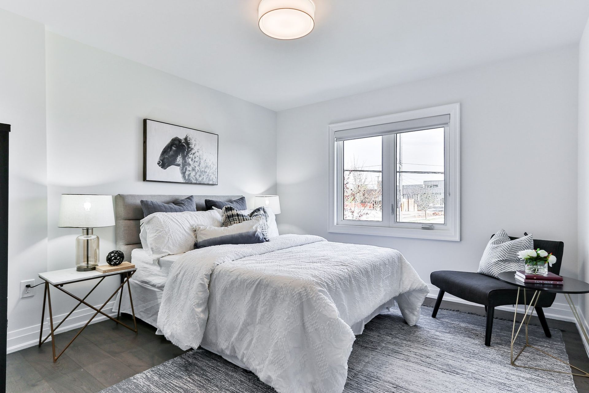 Bright gray bedroom with a bed, nightstands, window, and black bench on a shag rug