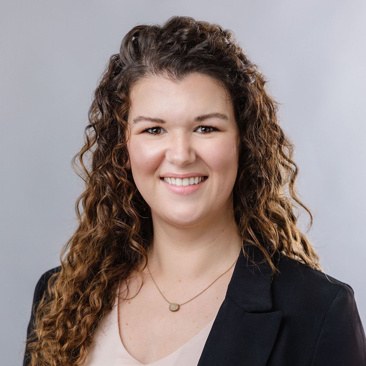 A woman with curly hair is wearing a black jacket and a pink shirt.