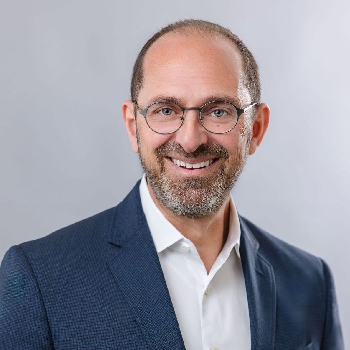 A man in a suit and glasses and is smiling for the camera .