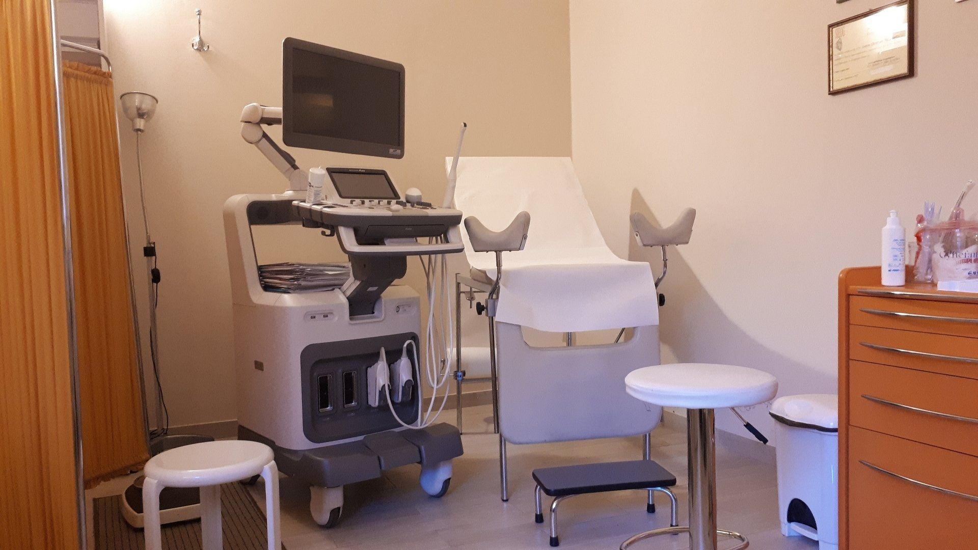 Sala ecografica con carrello medico, monitor, lettino imbottito, sgabello e armadietto.