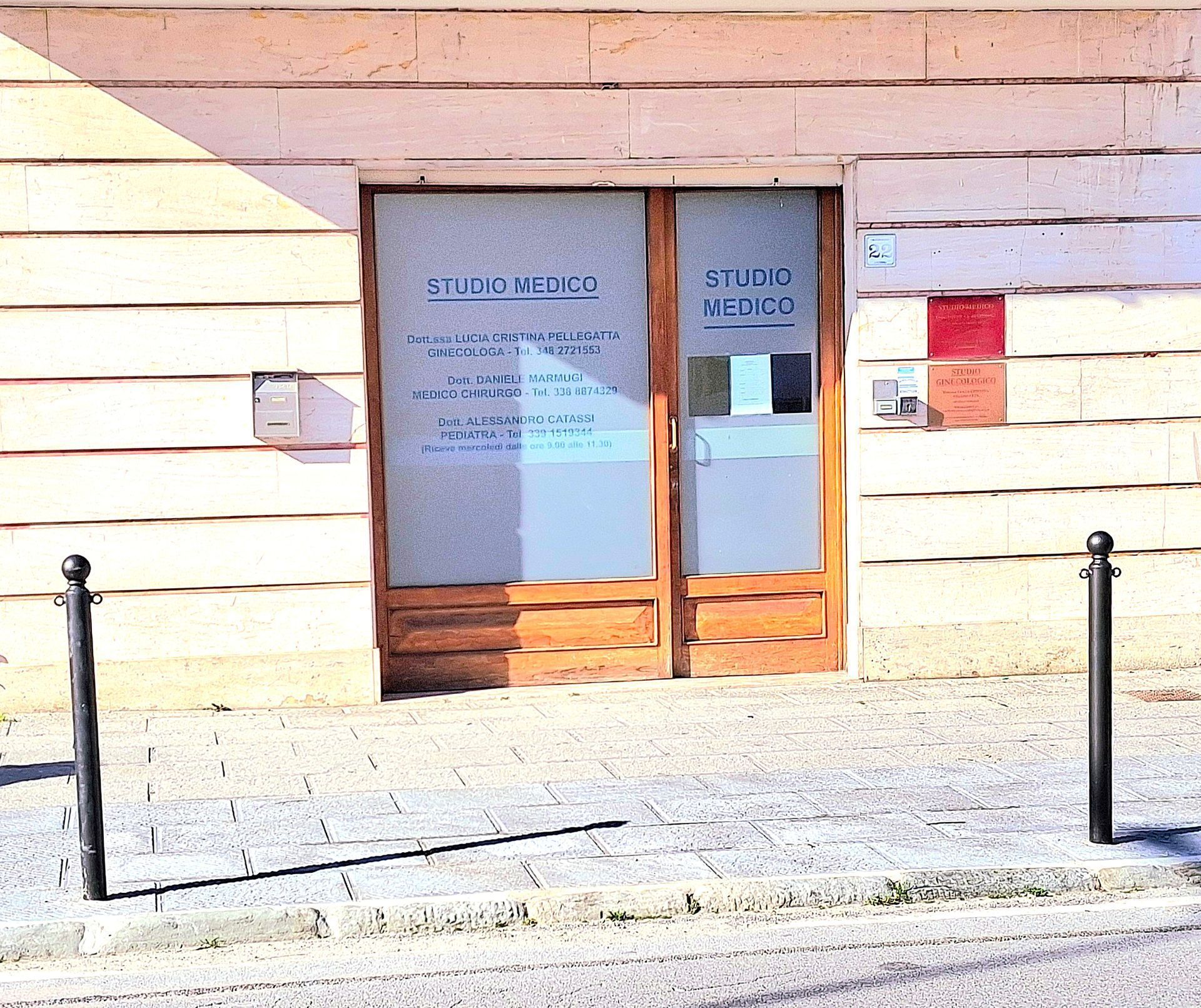 Vetrina con doppie porte a vetri, insegna e dissuasori neri davanti a un muro di mattoni chiari.