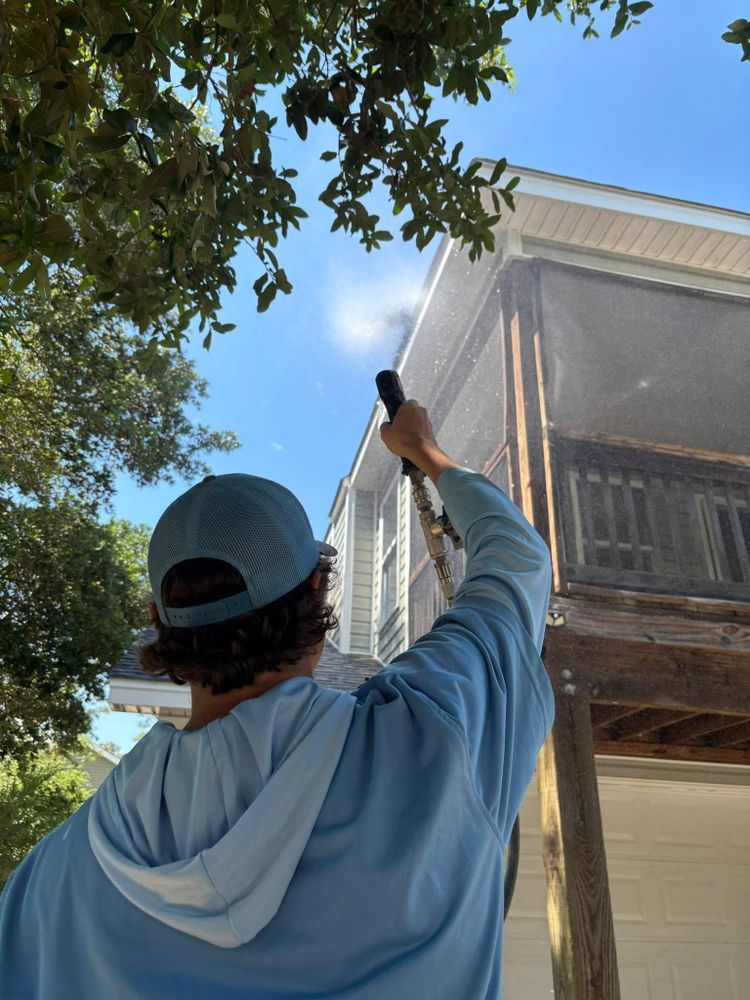 A man is cleaning the side of a house with a high pressure washer.