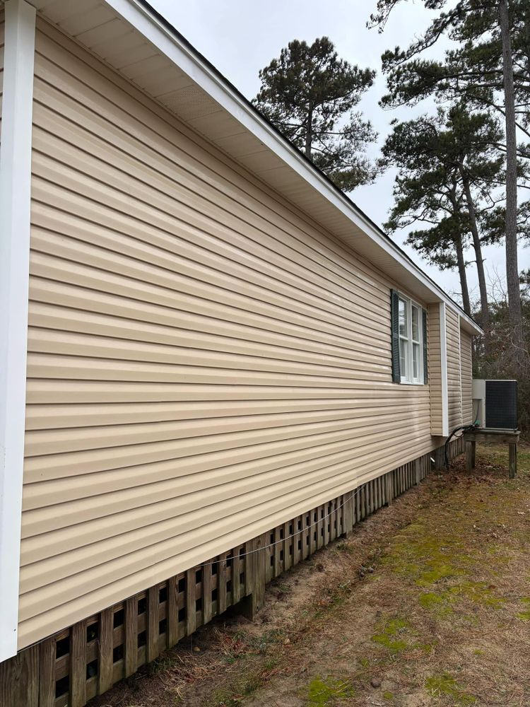 The side of a mobile home with a fence and trees in the background.