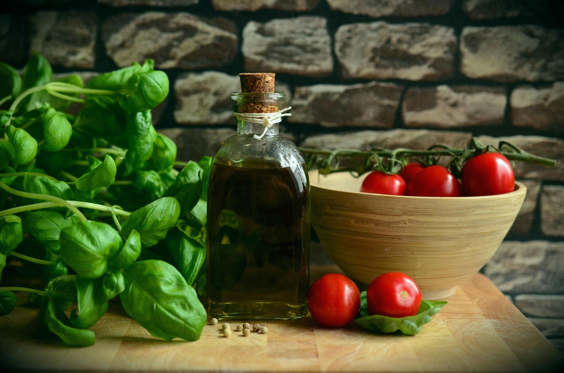 Basilico fresco, olio d'oliva e pomodori su una tavola di legno con sfondo di mattoni.