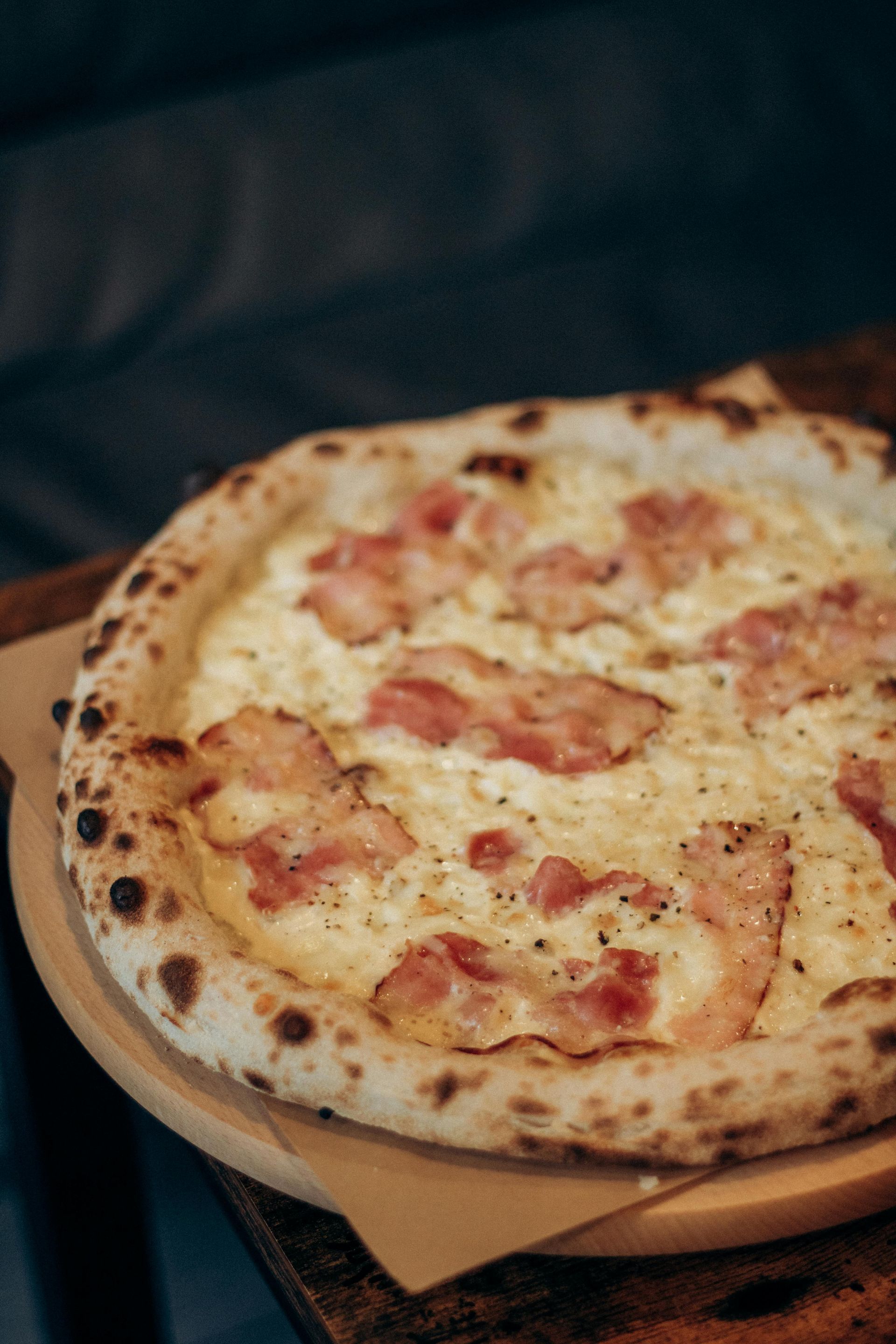 Pizza con besciamella e pancetta su un tagliere di legno.