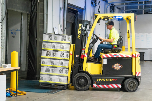 Forklift operator loading a pallet of boxes at a warehouse loading dock.