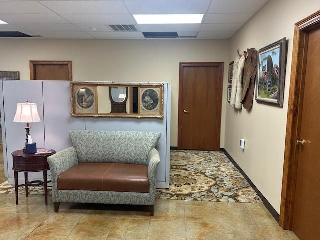 Office waiting area with sofa, rug, doors, paintings, and a table with a lamp.