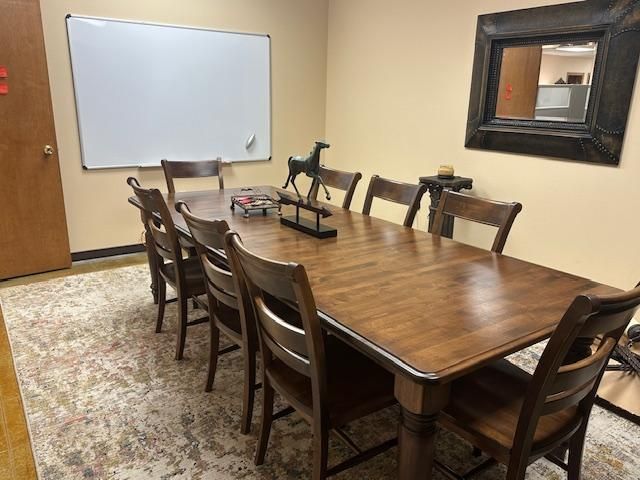 Wooden conference room table surrounded by chairs, with a whiteboard and mirror on the walls.