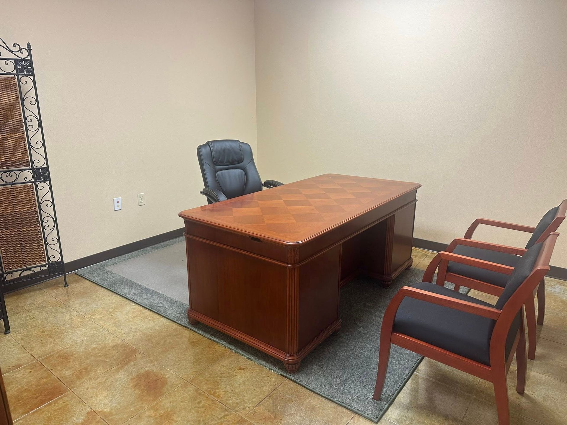 Office with a wooden desk, black office chair, two guest chairs, and decorative screen.