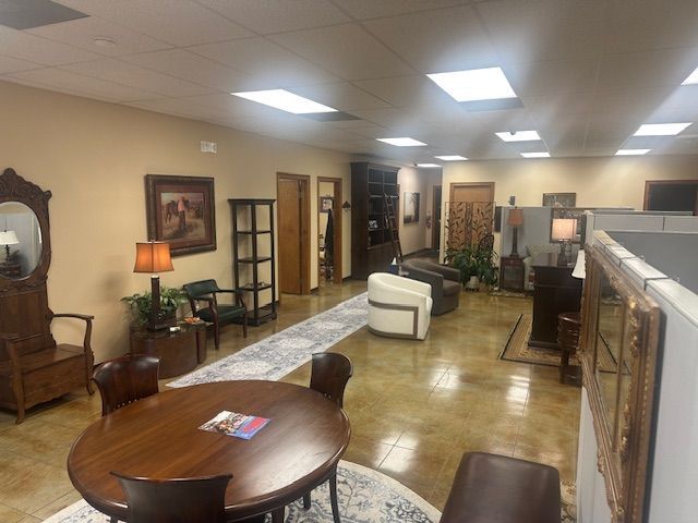 An office waiting area featuring a round table, armchairs, a rug, a tall shelving unit, and warm lighting.