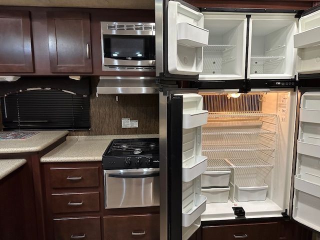 RV kitchen interior with empty refrigerator, microwave, stove, and cabinets.