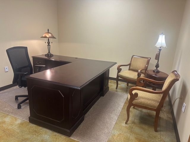 Dark wood office with desk, chairs, lamps, and beige walls.