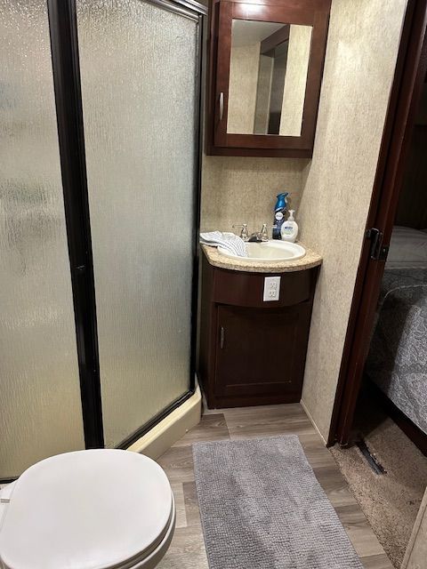 RV bathroom with a toilet, shower, vanity, and mirror. Brown cabinets and light gray floor.