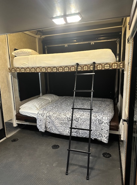 A bunk bed setup in a toy hauler garage, featuring a top bunk and a lower bed with a black metal ladder for access.