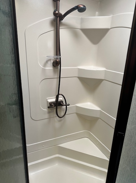 A corner shower unit with cream-colored molded plastic walls, integrated shelves, a built-in seat, and a handheld nozzle.