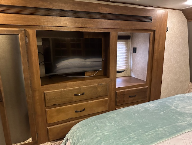 Wooden dresser with a TV built into a wall unit in a bedroom with a blue blanket visible in the foreground.