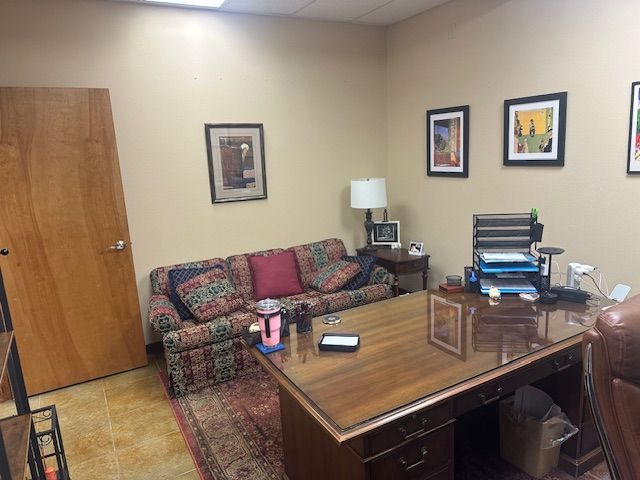 Office with a desk, couch, and framed artwork. The room has beige walls and a patterned rug.