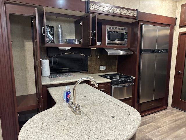 RV kitchen with island, cabinets, microwave, stove, and refrigerator.