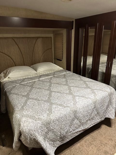 Bedroom in a recreational vehicle. A bed with patterned bedding and headboard, closet with mirrored doors.