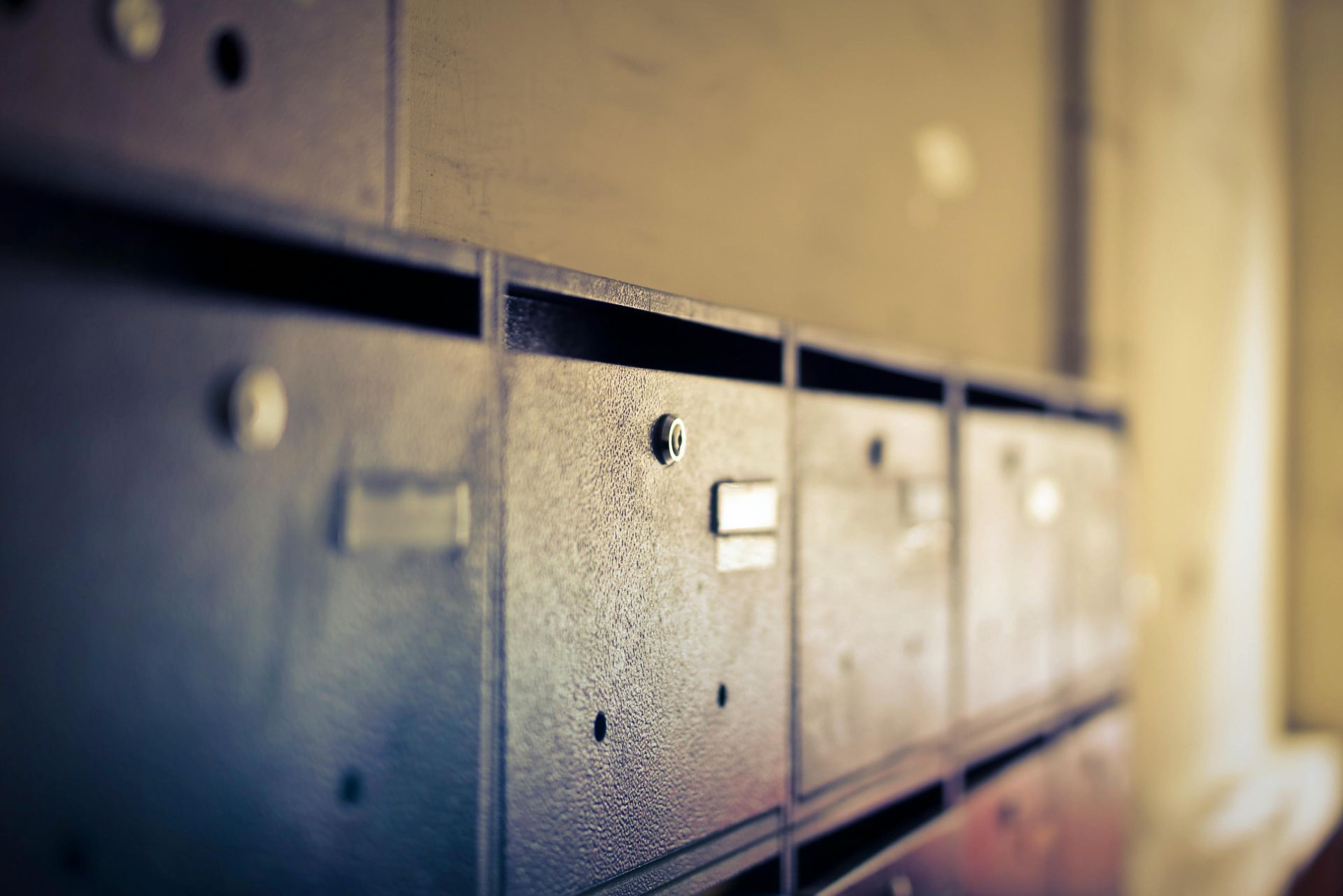 A close-up, angled view of a row of weathered, dark metal post office boxes in an indoor setting.