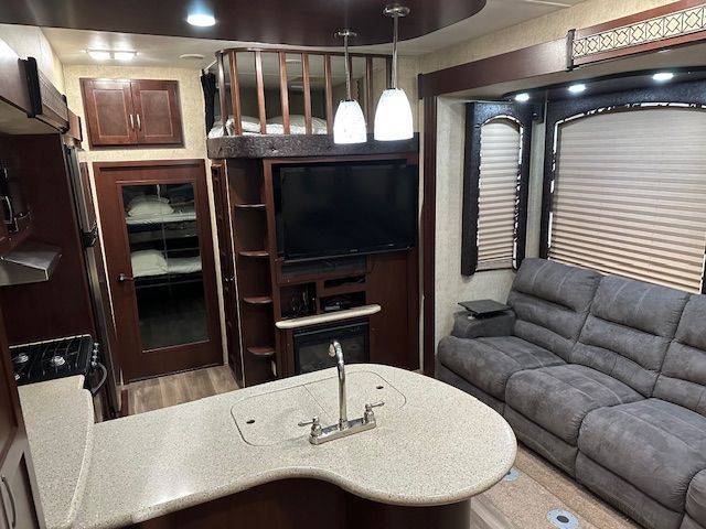 Interior view of a recreational vehicle with a kitchen, living area with sofa, and a loft bed.