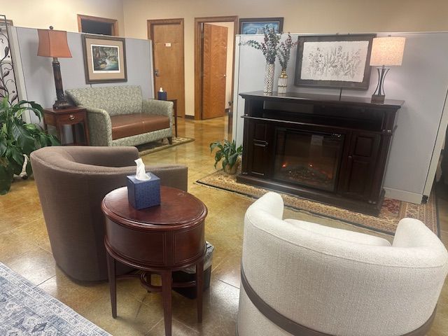 A waiting room featuring two armchairs, a loveseat, an electric fireplace, a side table with tissues, and office doors.