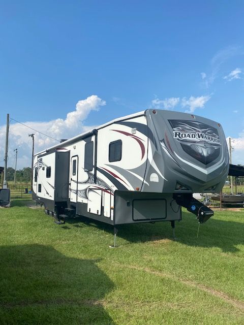 Gray and black Road Warrior RV parked on green grass under a blue sky.