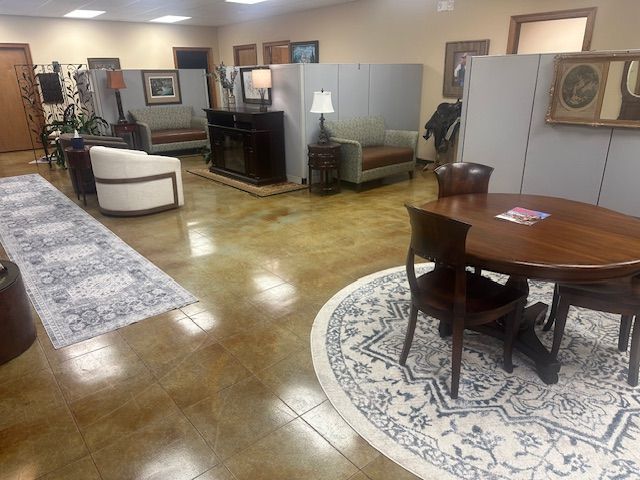 An office lobby with polished concrete floors, a round wooden dining set, a seating area with a white chair, and cubicles.