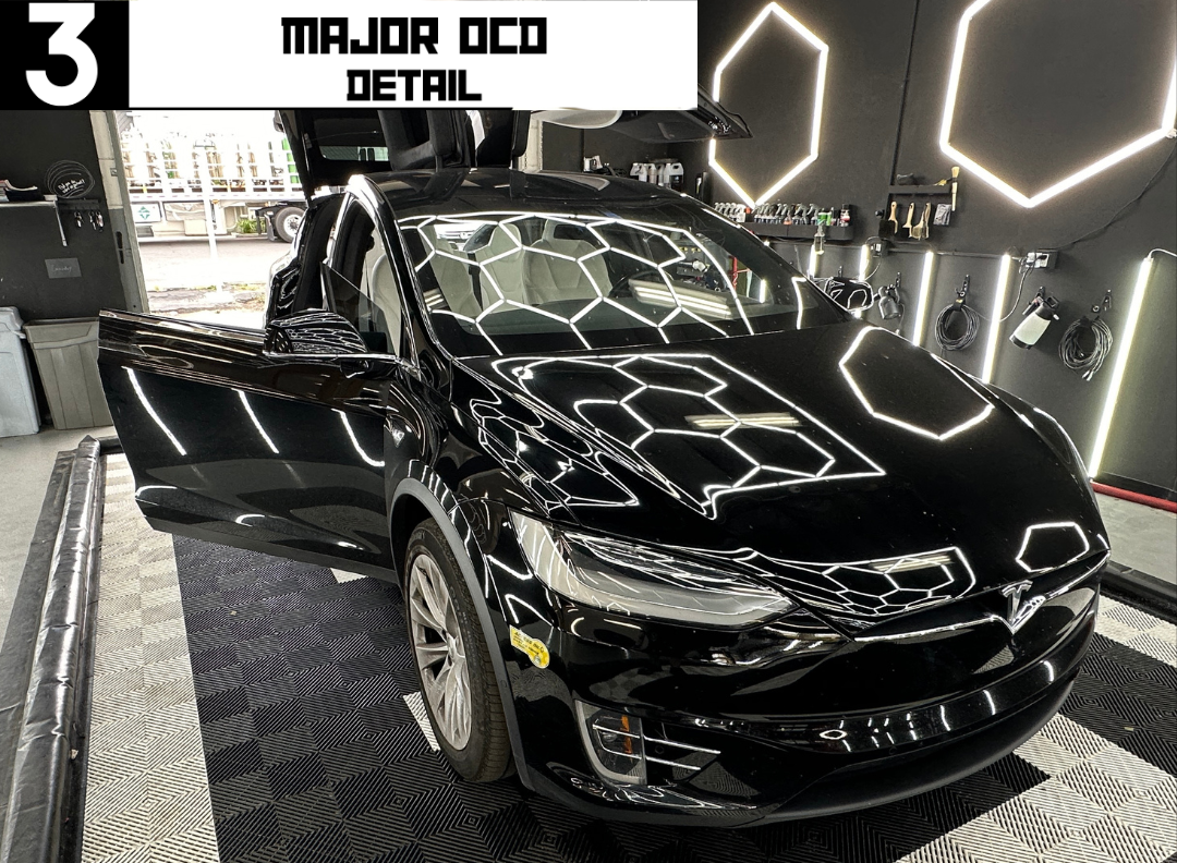 Black car with open doors in a detail shop, featuring bright lighting and reflection patterns.