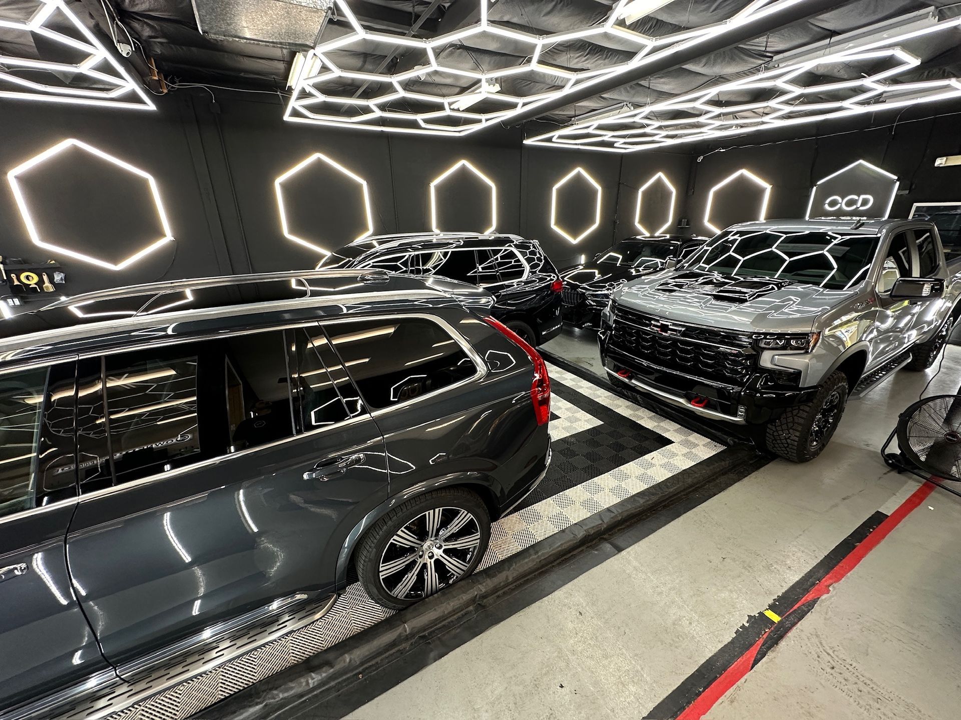 Cars in a detailing shop under hexagonal lights.