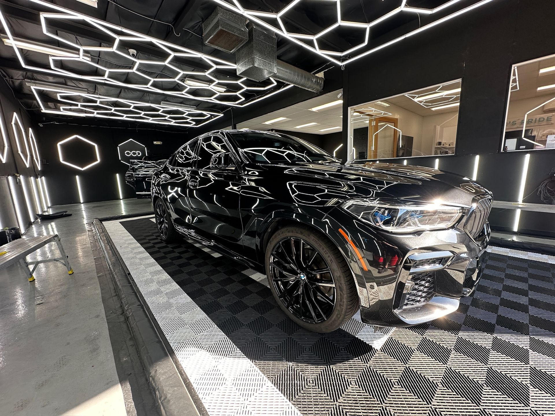 Black car in a garage with hexagon-shaped lights, black and silver floor tiles.