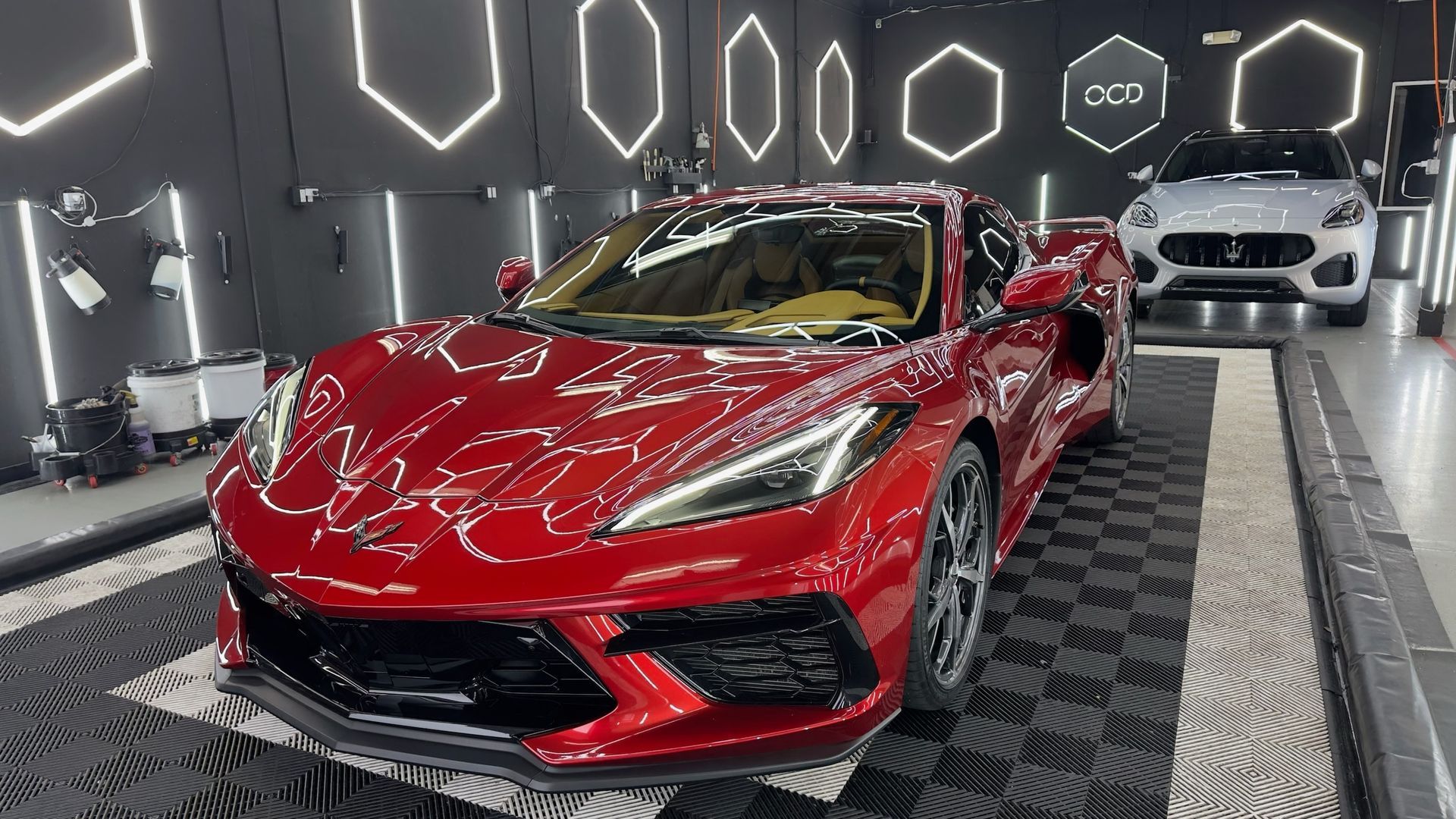 Red Corvette sports car in a detailing shop, with a white SUV in the background.