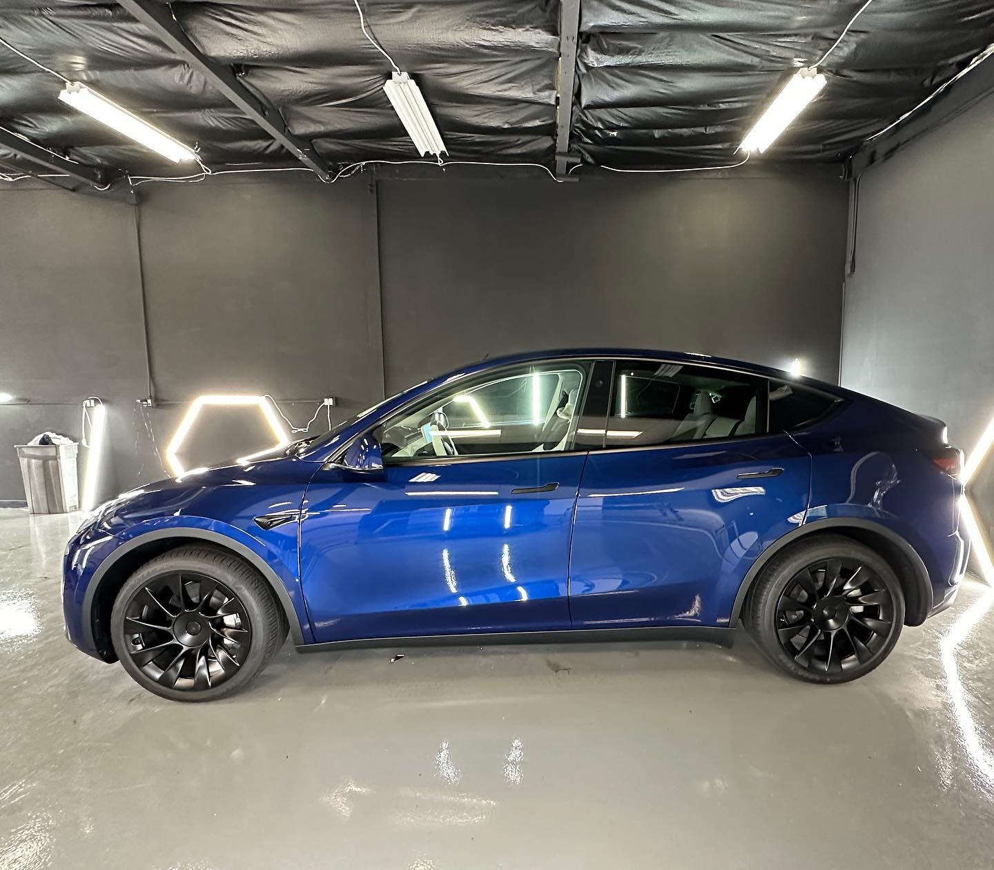 A blue tesla model y is parked in a garage.