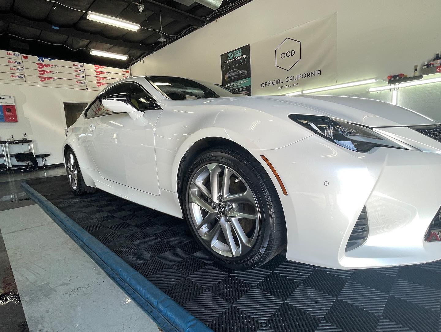 A white sports car is parked on a black mat in a garage.