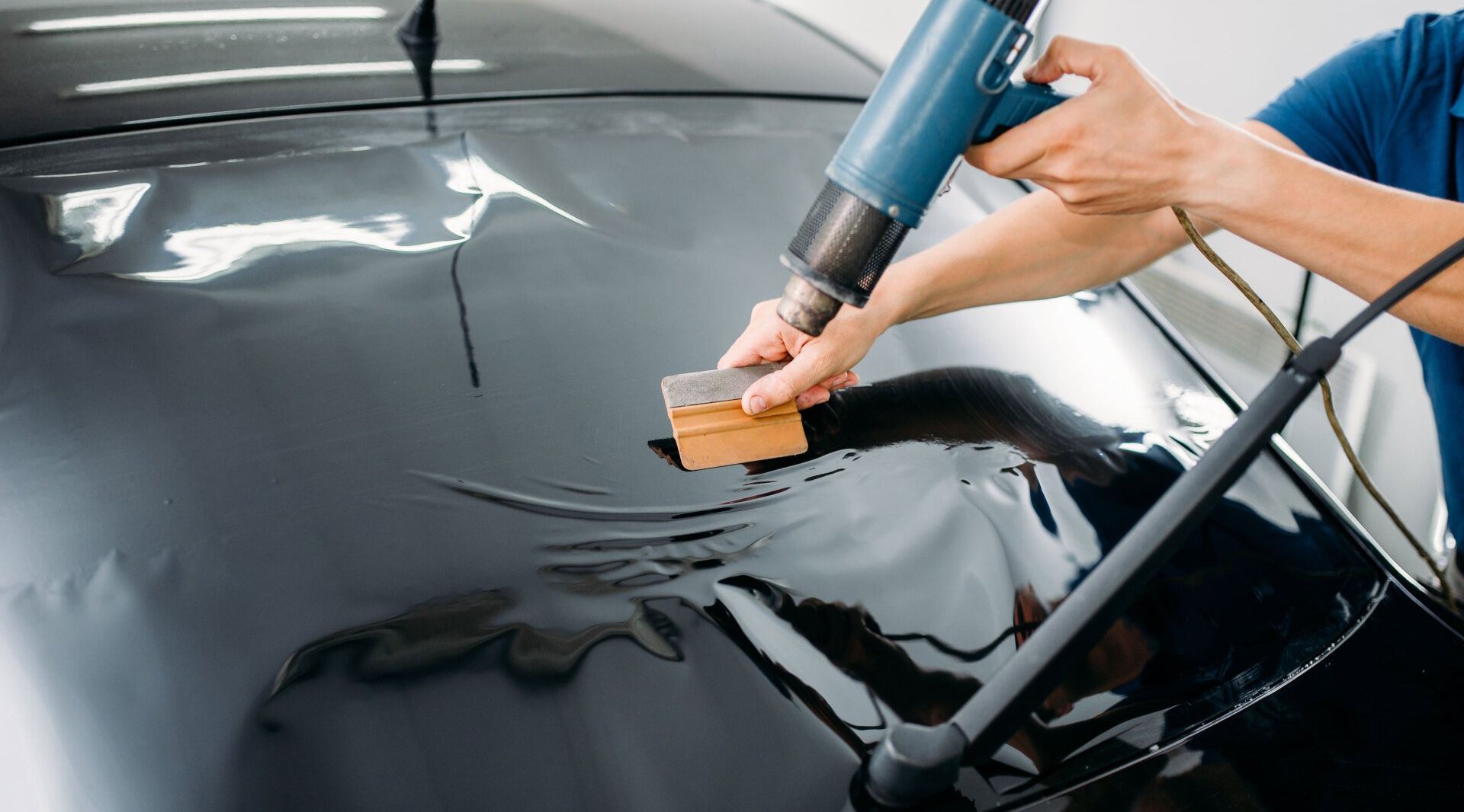 A person is applying tinted window film to a car.