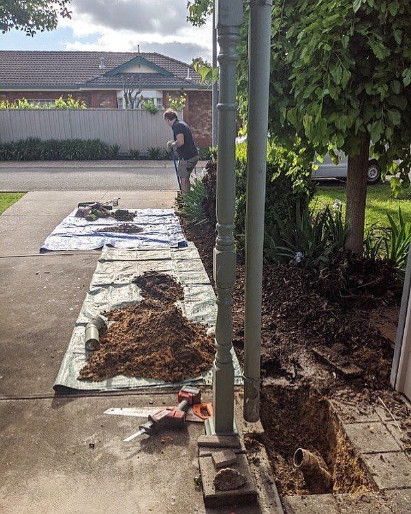 A man is digging a hole in the ground in front of a house.