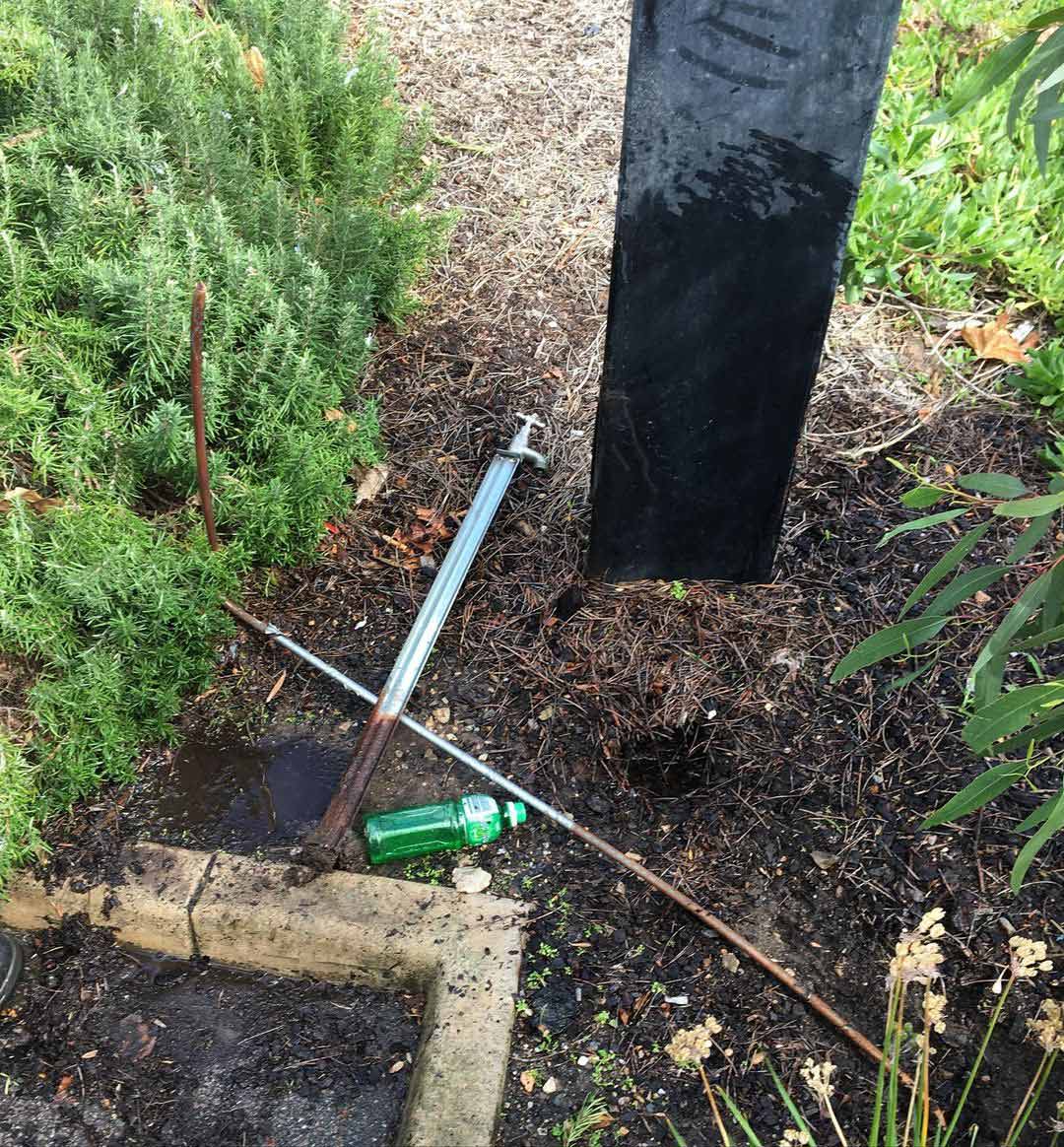 A green bottle is laying on the ground next to a screwdriver.