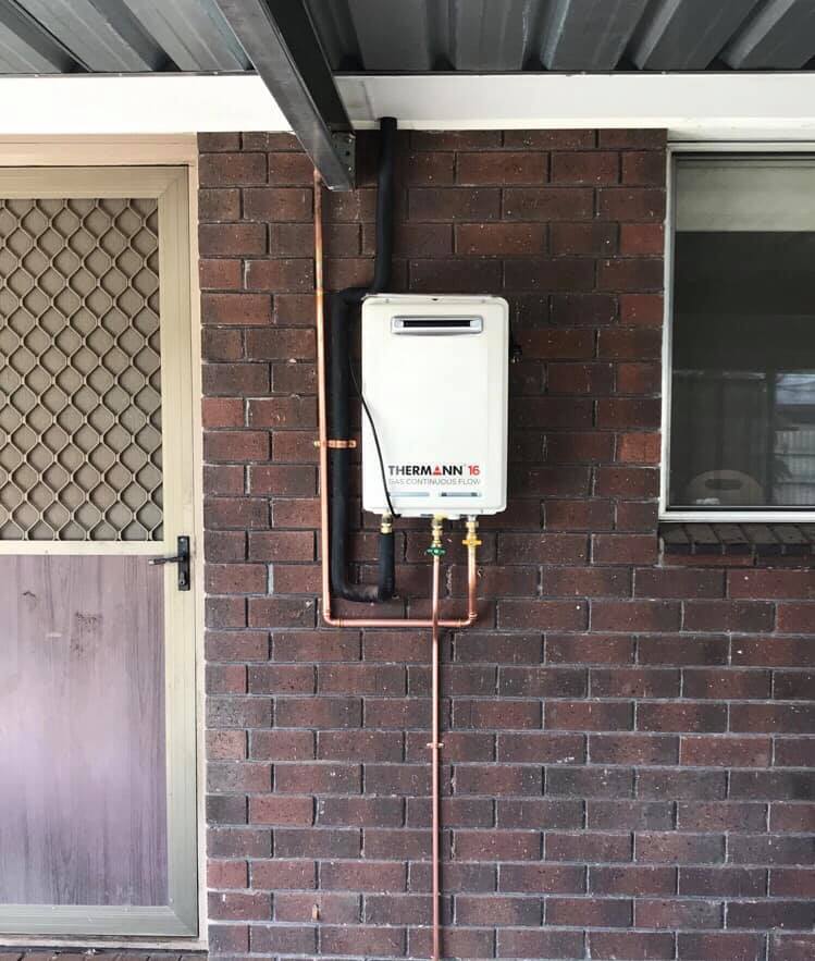 A brick wall with a water heater attached to it