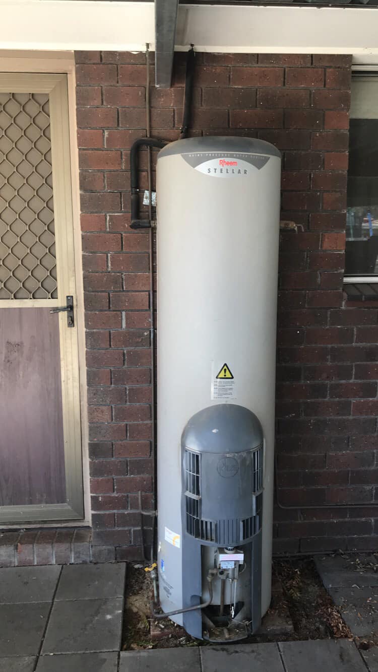 A water heater is sitting on the side of a brick building.