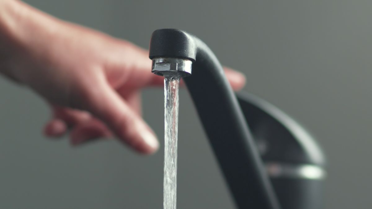 Hand turning off a black faucet, water flowing into a sink.