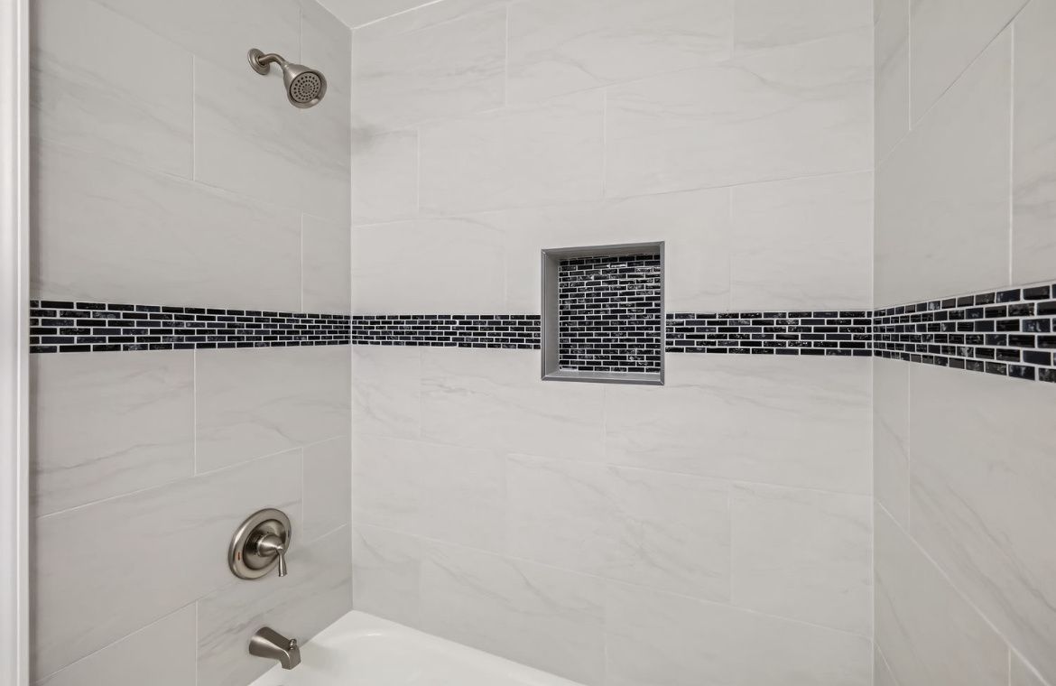 White tiled shower with black mosaic accent strip and wall vent.