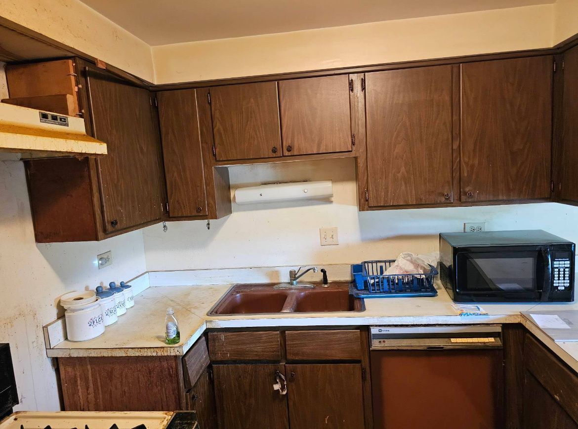 Small kitchen with dark wood cabinets, white counters, and a microwave on the right.