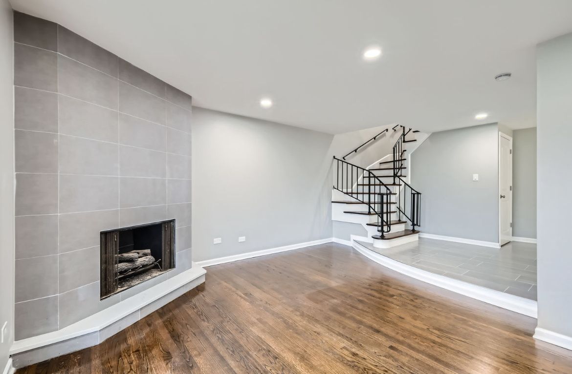 Spacious living room with fireplace, wood floors, gray walls, and a curved staircase.