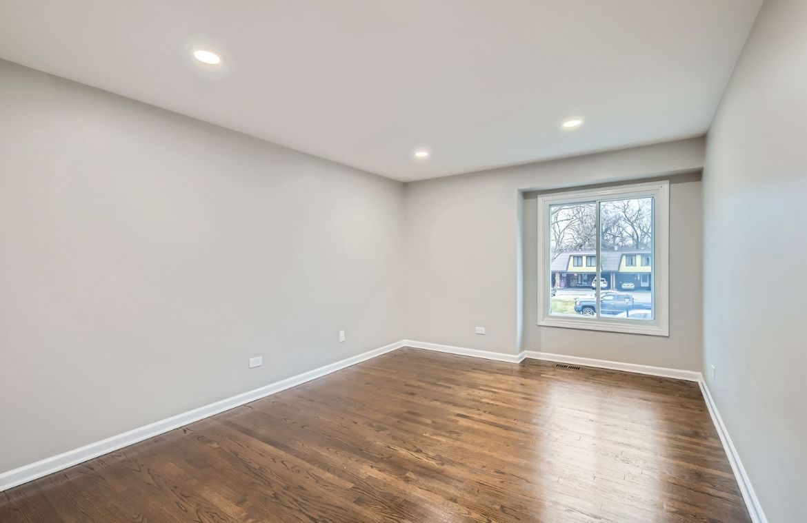 Empty modern room with gray walls, hardwood floor, and a window letting in daylight