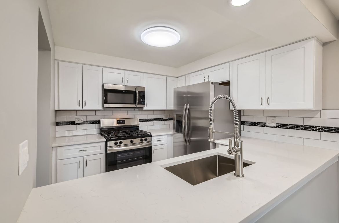 Bright white modern kitchen with stainless steel appliances, island sink, and light gray walls