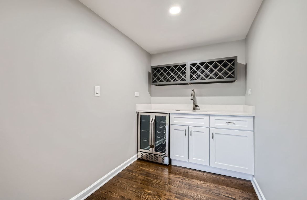 Small kitchenette with white cabinets, sink, mini fridge, and dark wood floor in a narrow room