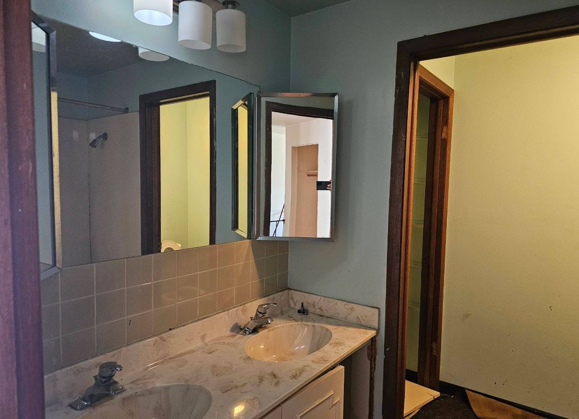 Small bathroom vanity with mirror, sink, tiled backsplash, and open door to a hallway.