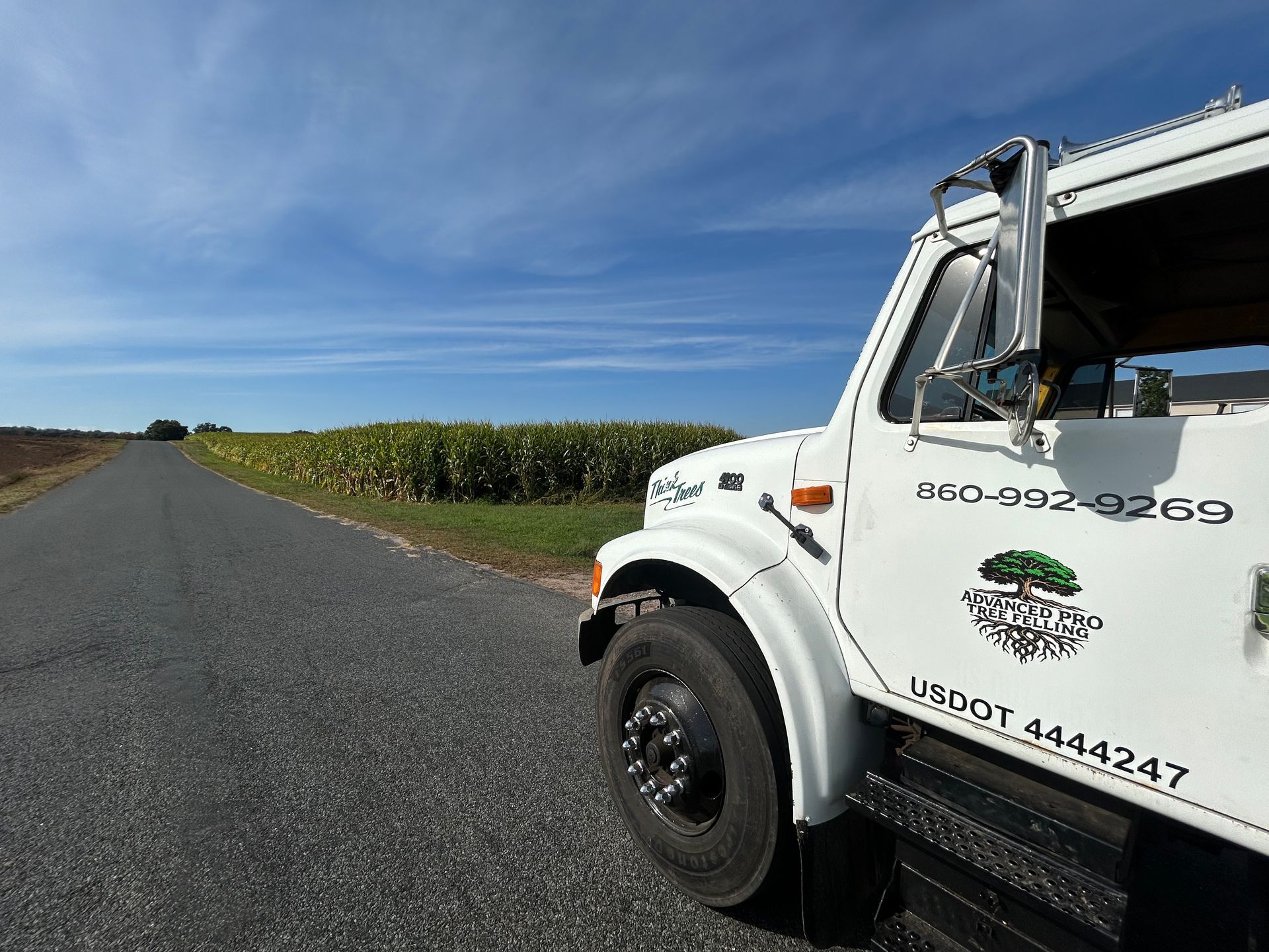 White utility truck on a rural road beside fields under a blue sky