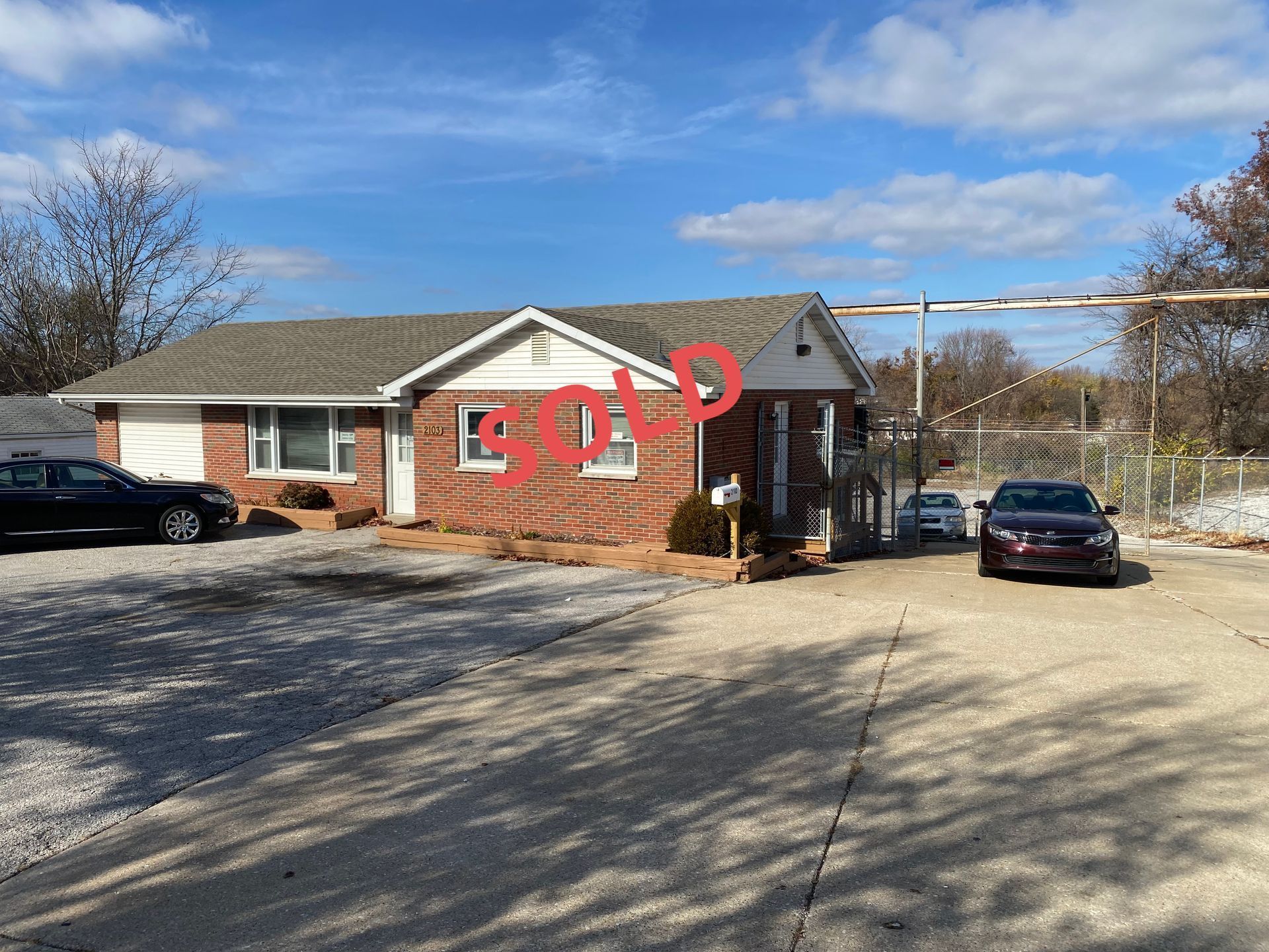 A brick house is for sale with cars parked in front of it.
