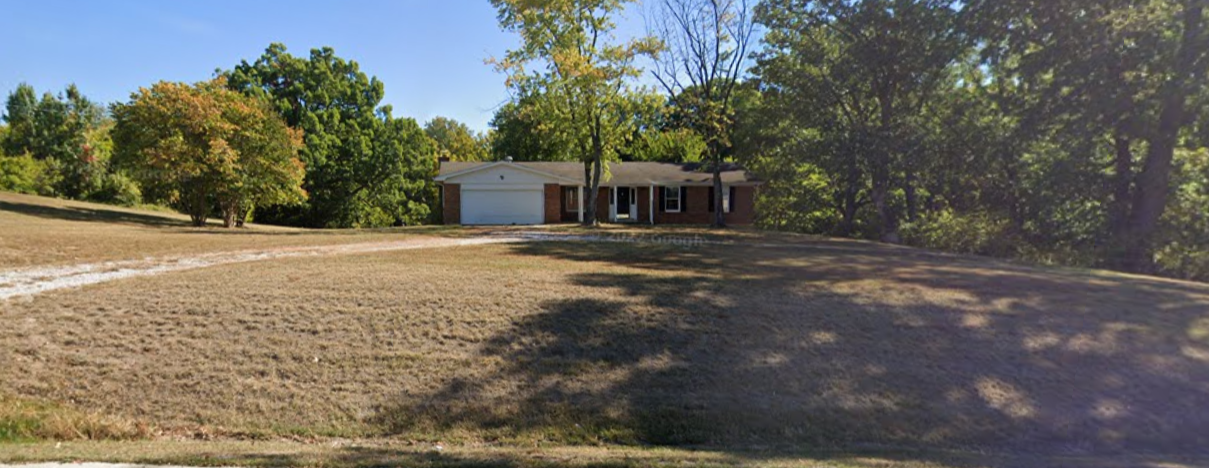 A house is sitting in the middle of a field surrounded by trees.
